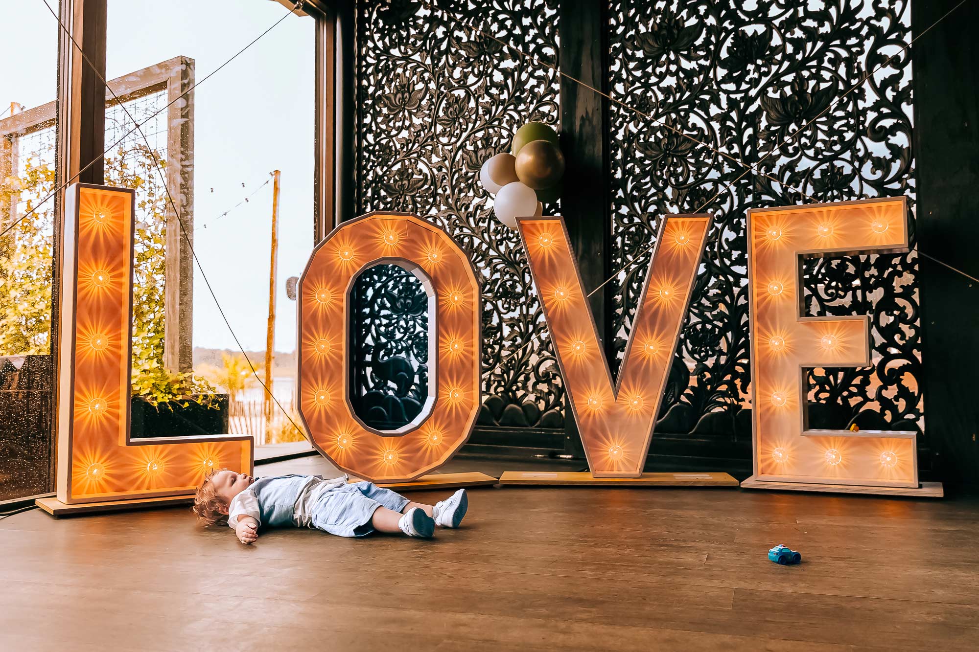 Een peuter is klaar met de bruiloft en ligt op het podium voor de lichtletters LOVE op de grond.