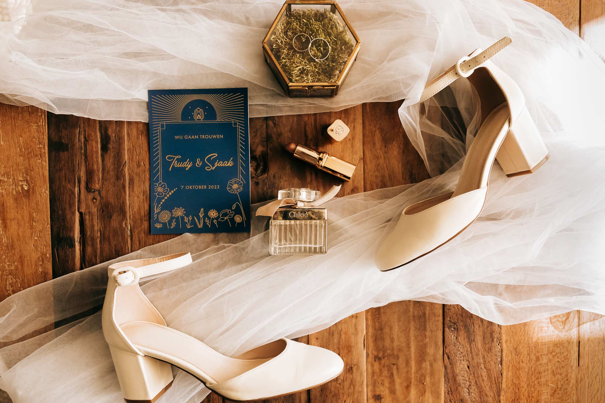 Een flatlay van de accessoires van de bruid op de dag van de bruiloft. Trouwschoenen, trouwringen, trouwkaart maar ook de make-up en parfum mogen niet ontbreken.