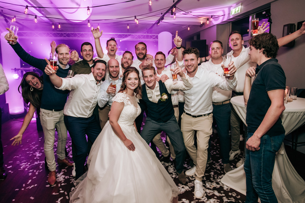 Een grote groepsfoto met het bruidspaar met vrienden tijdens het trouwfeest in Gilze (Noord-Brabant).